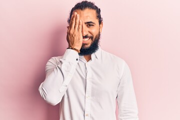 Young arab man wearing casual clothes covering one eye with hand, confident smile on face and surprise emotion.