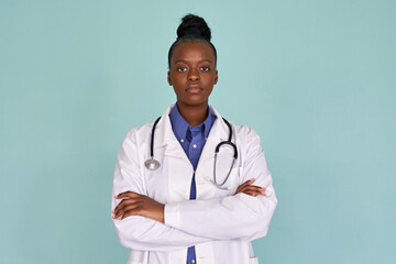 Confident african female doctor wear white lab coat, stethoscope look at camera stand on mint green studio background. Serious proud black woman professional therapist physician arms crossed portrait.