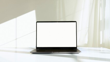 A photo of a laptop on a white desk with a white wall