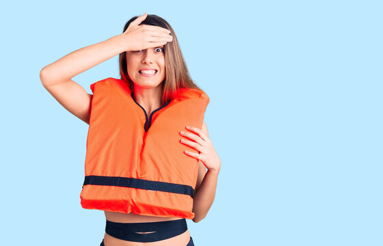Young beautiful girl wearing life jacket stressed and frustrated with hand on head, surprised and angry face