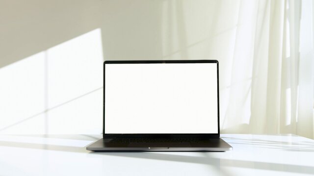 A photo of a laptop on a white desk with a white wall