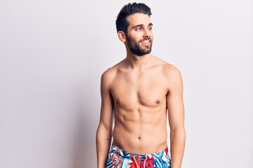 Young handsome man with beard shirtless wearing swimwear looking to side, relax profile pose with natural face and confident smile.