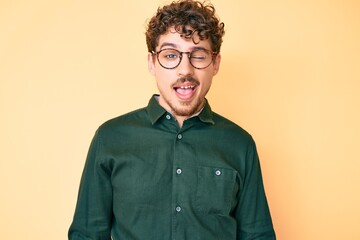 Young caucasian man with curly hair wearing casual clothes and glasses winking looking at the...