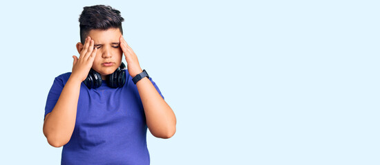 Little boy kid listening to music wearing headphones with hand on head for pain in head because stress. suffering migraine.