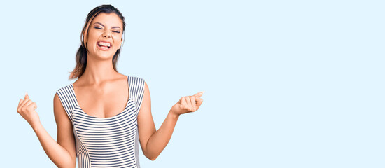 Naklejka na ściany i meble Young beautiful woman wearing casual dress very happy and excited doing winner gesture with arms raised, smiling and screaming for success. celebration concept.