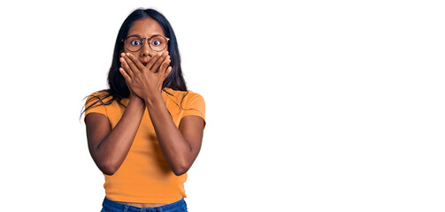 Young indian girl wearing casual clothes and glasses shocked covering mouth with hands for mistake....