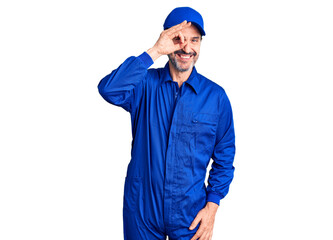 Middle age handsome man wearing mechanic uniform doing ok gesture with hand smiling, eye looking through fingers with happy face.