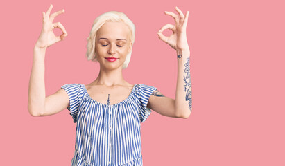 Young blonde woman with tattoo wearing casual clothes relax and smiling with eyes closed doing meditation gesture with fingers. yoga concept.