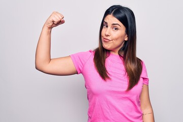 Obraz na płótnie Canvas Young beautiful brunette woman wearing casual pink t-shirt standing over white background Strong person showing arm muscle, confident and proud of power