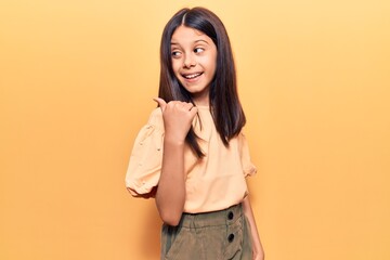 Beautiful child girl wearing casual clothes smiling with happy face looking and pointing to the side with thumb up.