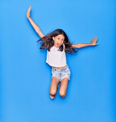 Adorable hispanic child girl wearing casual clothes smiling happy. Jumping with smile on face over isolated blue background