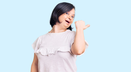 Brunette woman with down syndrome wearing casual white tshirt smiling with happy face looking and pointing to the side with thumb up.