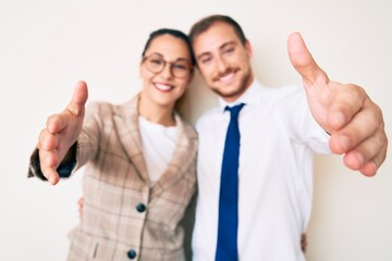 Beautiful couple wearing business clothes looking at the camera smiling with open arms for hug. cheerful expression embracing happiness.