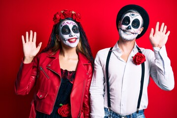 Couple wearing day of the dead costume over red waiving saying hello happy and smiling, friendly welcome gesture © Krakenimages.com