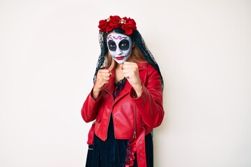 Woman wearing day of the dead costume over white ready to fight with fist defense gesture, angry and upset face, afraid of problem