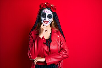 Woman wearing day of the dead costume over red looking confident at the camera with smile with crossed arms and hand raised on chin. thinking positive.