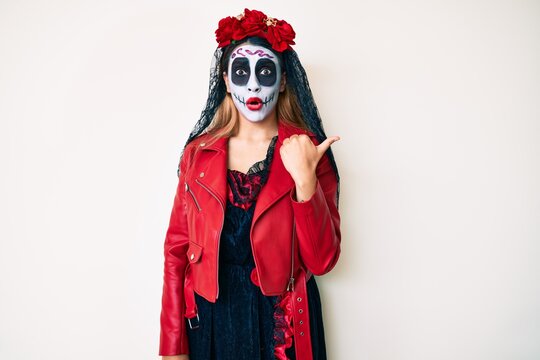 Woman wearing day of the dead costume over white surprised pointing with hand finger to the side, open mouth amazed expression.