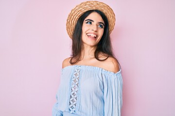 Brunette teenager girl wearing summer hat looking away to side with smile on face, natural expression. laughing confident.