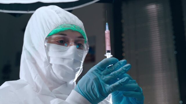 People vaccination concept, medical worker in protective uniform filling syringe with potential vaccine against coronavirus infection. Virologist researcher in laboratory