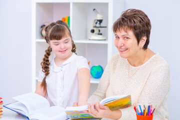 Down syndrome girl with thick dark hair reading a book with her teacher while sitting in a lesson in the classroom Education accessible to children with disabilities concept