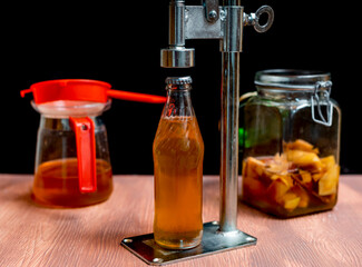 Bottling homemade fermented kombucha using a manual bottle capping machine. Second fermented kombucha with apples and cinnamon at background. Isolated on black. Kombucha tea is popular healthy drink.
