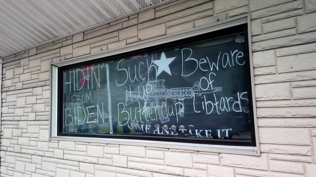 Political handwritten sign, saying, white letters and standpoint written on glass window of brick front store voicing opinion, handheld close up pan forward