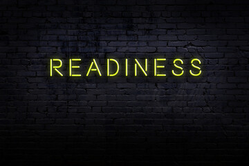Neon sign. Word readiness against brick wall. Night view