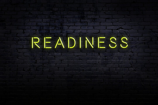 Neon sign. Word readiness against brick wall. Night view