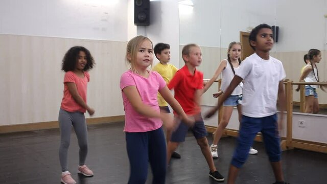 Preteen boys and girls with female trainer practicing floss dance movements, swinging hips and arms during group class. High quality FullHD footage