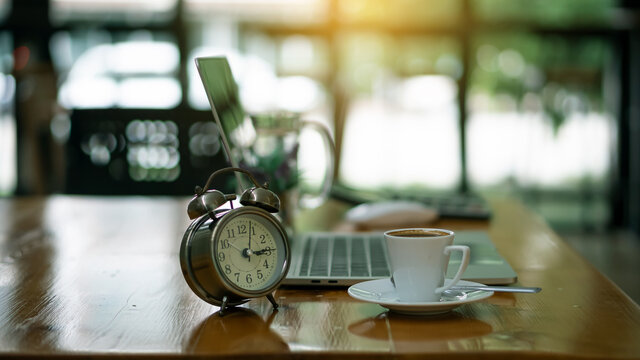 Coffee cups and clocks are placed next to the laptop on the wooden table in the office.