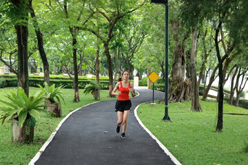 Relaxed smiling Asian fitness runner woman listening music and running workout in natural park.