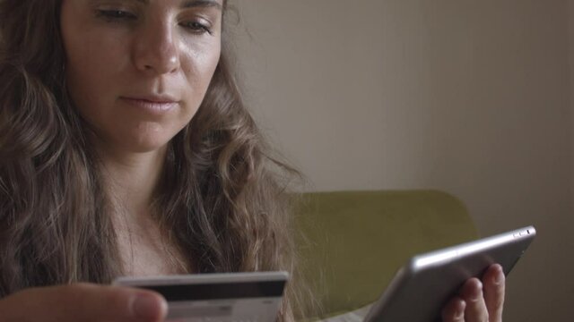 Young caucasian woman using master card and digital tablet while shopping at home. Woman shopping at home. Woman buys online.