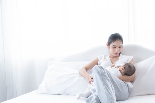 Mother Breastfeeding Her Newborn Baby Beside Window. Milk From Mom’s Breast Is A Natural Medicine For Children. Woman Feeding Baby. A Young Mother Holding Her Baby Child. .