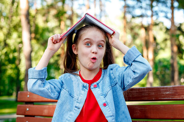 Cheerful smiling teen girl with book on her head in park having fun. Looking at camera. School...