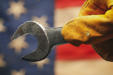 Worn work glove holding wrench tool above US American flag. Made in USA, American workforce, blue collar worker, or Labor Day concept.