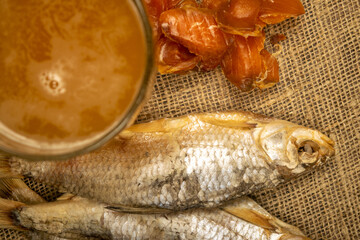 Dried fish, dried caviar and a beer mug on a homespun cloth with a rough texture. Close up.
