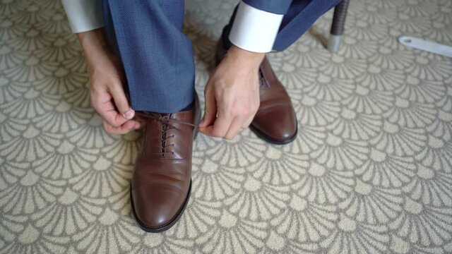 a man tying laces on brown leather shoes. groom puts on shoes.