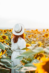 young woman in sundress walking by sunflowers field on sunset