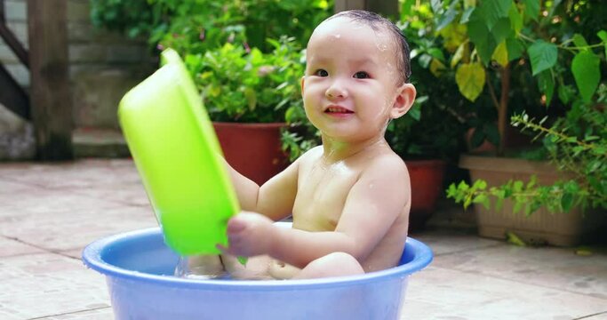 little asian baby girl sitting in the basin playing water take bath in the yard at summer afternoon little girl playing hide and seek 