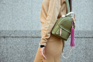 Fashion woman wearing knit pants and knit sweater. She is holding beige leather backpack on her shoulders. Street style. 