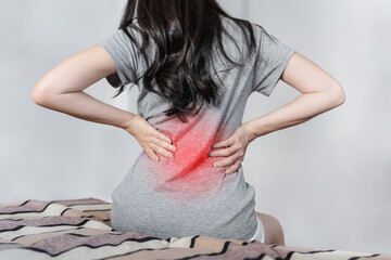 Backache and Lower back pain concept. Young woman suffering from back pain, on bed after waking up