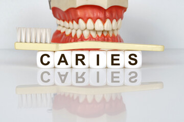 Medical, dental concept. The text is written on the cubes - CARIES. In the background is a model of the jaw, with a toothbrush on the cubes.