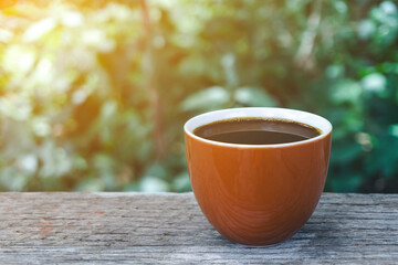 Hot coffee big cup Ceramic brown glass placed on an outdoor wood table. The background is a green tree nature with orange light