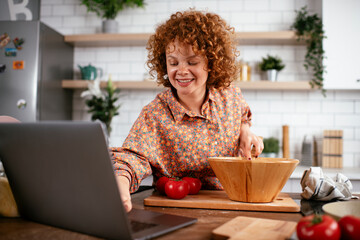 Young woman is reading a recipe while cooking. Beautiful woman with curly hair enjoying in the kitchen.