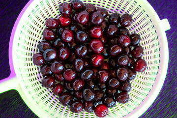 Ripe juicy cherries in plastic colander. Organic red sweet cherries on dark neon-lit background.
