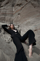 Fashion sexy woman in a suit posing on sand rocks. Modern independent girl, beautiful makeup