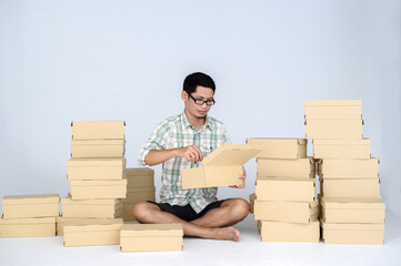 Asian man packing goods for selling online among many boxes with parcels on a white background. Concept of freelance startup and online business home office.