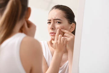 Fototapeta na wymiar Young woman with acne problem squishing pimples near mirror