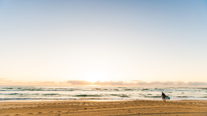 Fototapeta na wymiar a surfer on the beach silhouette surfboard early morning