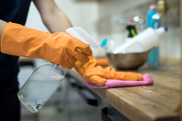 woman in rubber gloves and cleaning the kitchen counter with sponge